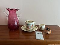 Group shot showing all five items: cranberry vase, Bunnykins teacup, saucer, mug, and dog figurine