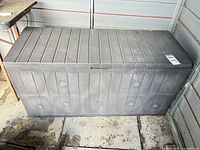 Closed grey deck box showing exterior slat pattern, detached lid resting on top