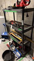 Front view of four-tier black plastic shelving unit with tools shown for scale