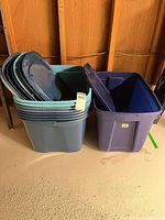 Stack of eight blue 63 L totes nested together alongside single dark blue 76 L tote, lids shown