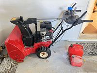 Full view of Toro snow blower with two red gas cans