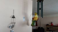 Wide view showing ceramic parrot on brass ring, Arias wind chime above, dolphin wind chime on wall