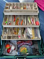 Open tackle box showing trays with assorted lures, hooks, bobbers and soft plastics