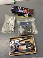 Staple gun, sanding belts pack, two bags of hardware displayed on table