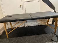 Full view of black portable massage table on wooden legs