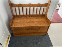 Front view of closed oak storage bench highlighting spindle backrest and curved arms