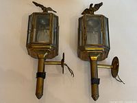 Front view of both brass wall lanterns showing overall design, glass panels, eagle finials and wall arms