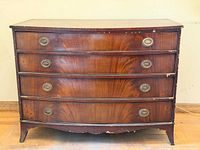 Front view showing bow front, four drawers, brass pulls, veneer chips