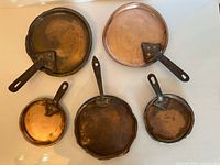 Top view of all five copper pan lids showing copper tops and iron handles