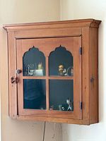 Full view of wall-mounted pine corner cabinet showing door, knob, hinges, glass panels, and overall shape