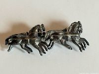 Front view of brooch showing two galloping horses and pin mechanism