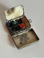 Open paint box showing eight colour pans and hinged lids