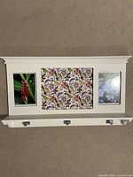 Front view of white wall-mounted coat rack showing photo frame openings and shelf