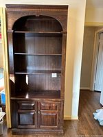 Full front view of tall dark brown bookcase-cabinet showing three open shelves and lower two-door cabinet