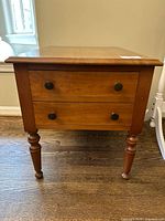 front view showing two drawers with brass knobs and turned legs