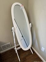 Full view of white oval cheval mirror standing against wall