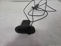 Front view showing lens, microphone grille, logo, privacy strap and cable