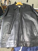 Front view of black leather jacket showing zipper, collar, and front welt pockets