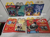 Front view of six unfolded Happy Meal cartons showing graphics for Jungle Book, Halloween, Kung Fu Panda 2 and Young Justice