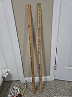Both wooden yardsticks leaning against wall