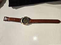 Watch laid flat showing emblem on back and brown leather strap