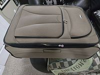 Top view of tan WestJet suitcase showing front pocket, logo badge and zippers