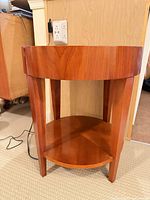 Front view of cherry veneer round side table displaying top surface, legs and lower shelf