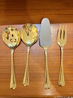 Four gold-tone serving pieces: slotted spoon, serving spoon, pie server, serving fork