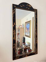 Full view of vertical black and gold chinoiserie wall mirror mounted on wall