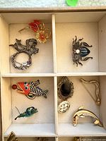 Front view showing six brooches including floral spray, wreath, spider, fish, snake, dolphin