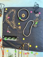Overview of multiple necklaces on dark cloth: metal chains, coil choker, mesh chain, bead cuff