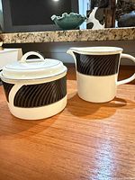 sugar bowl with lid alongside matching creamer showing black stripe band pattern