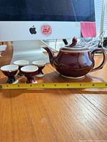 Teapot with lid and four cups next to tape measure showing scale