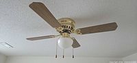 Ceiling-mounted 42-inch polished brass fan with four oak-tone blades and globe light