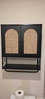 Front view of wall-mounted cabinet showing doors with rattan panels and lower shelf/towel bar