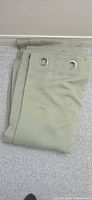 Folded sage green curtain panels showing grommet tops