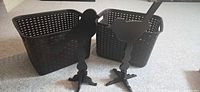 Two brown plastic baskets and two black wooden bird stands displayed together