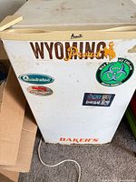 Front and top view of white Avanti compact refrigerator showing stickers, power cord, and surface wear