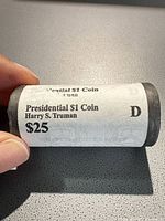 Paper-wrapped roll labeled 'Presidential $1 Coin Harry S. Truman $25 D' held in hand