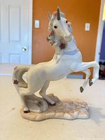 Front view of porcelain unicorn figurine on base showing floral details and gold accents