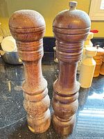 Two tall wooden pepper mills with wear