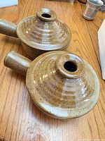 Top view of two stoneware handled crocks with lids on showing speckled glaze and steam vents