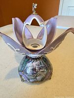 Full view of porcelain music box with open flower petals and cherub finial