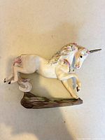 Right-side view of porcelain unicorn figurine showing floral accents, gold horn, hoof tips, and faux wood base