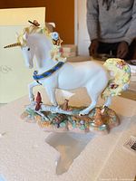 Full view of porcelain unicorn statue showing gold horn, multicolor mane, butterflies, woodland base with animals