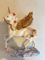 Left profile of porcelain unicorn-pegasus showing gold wings, horn, roses, cloud base