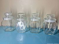 Front view of the four clear glass apothecary jars standing side by side