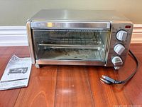 Front view of Black+Decker toaster oven with manual beside it