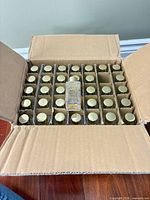 Open cardboard case showing grid of toner bottles with gold caps, one slot empty
