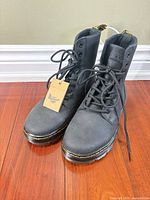 Front three-quarter view of both boots showing black leather, laces, yellow stitching, and hang tag